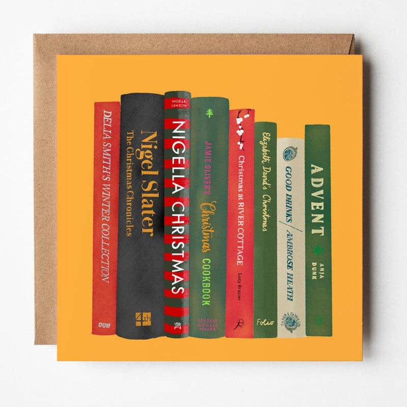 A square greeting card with a bright orange background featuring illustrated book spines in red, black, green, and blue, shown with a brown envelope behind it on a light gray background.
